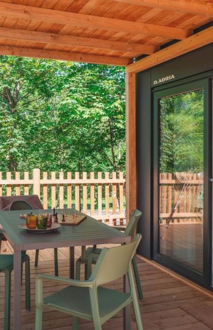 Terrazza in legno con tavolo, sedie e vista sul bosco.