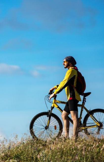 Radfahrer auf Hügel mit gelbem Fahrrad, blauer Himmel.