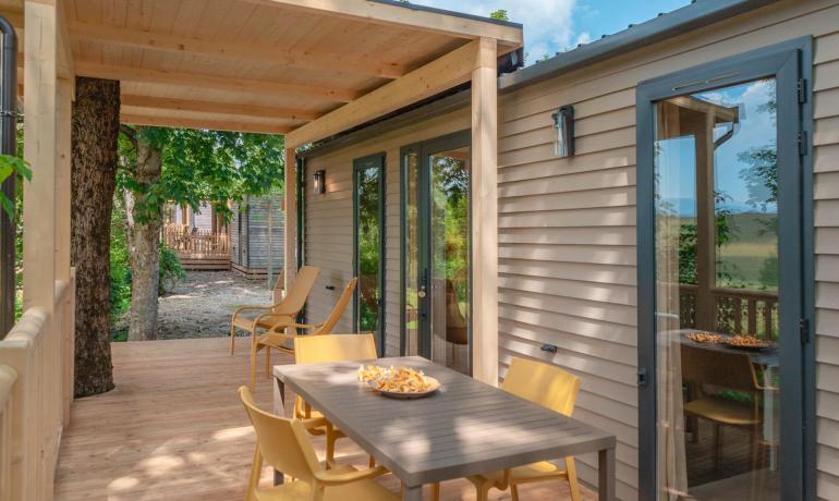 Holzterrasse mit gelbem Tisch und Stühlen, umgeben von Natur.