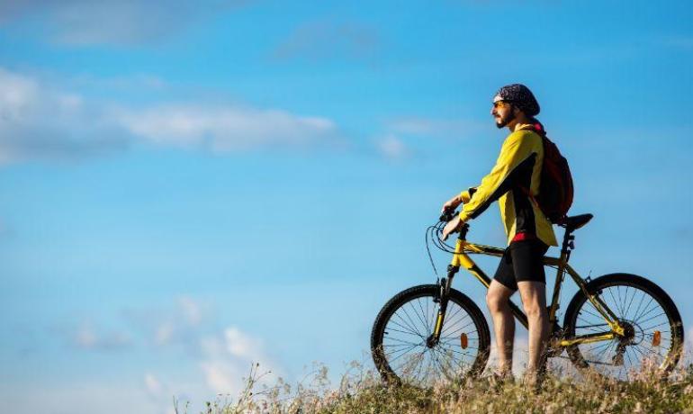 Radfahrer auf Hügel mit gelbem Fahrrad, blauer Himmel.