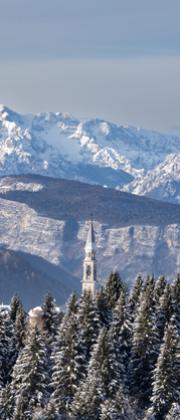 Paesaggio montano innevato con chiesa tra gli alberi.