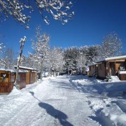 Strada innevata tra casette di legno in un paesaggio invernale.