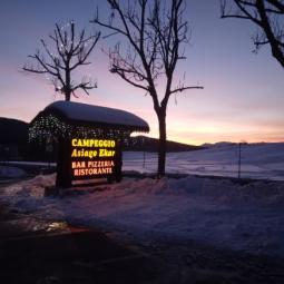 Campeggio Asiago Ekar al tramonto, con neve e luci natalizie.