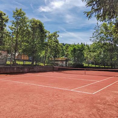 Campo da tennis su terra rossa in un'area verde.