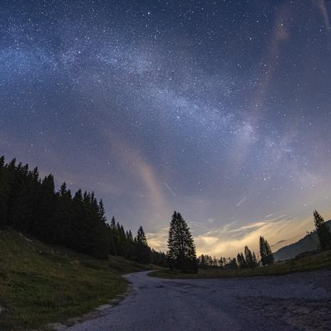 Strada di montagna sotto un cielo stellato e la Via Lattea.