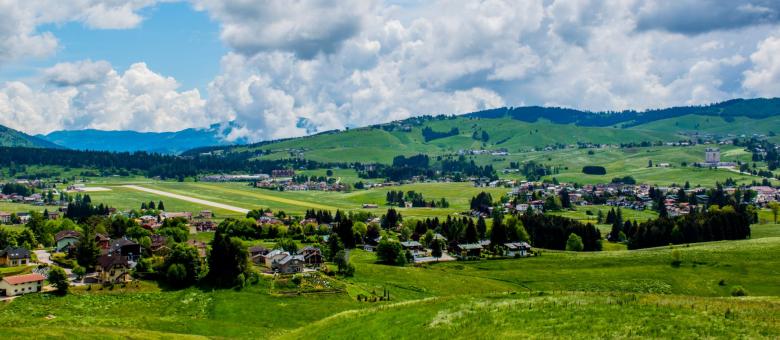 Paesaggio collinare con villaggio, prati verdi e cielo nuvoloso.