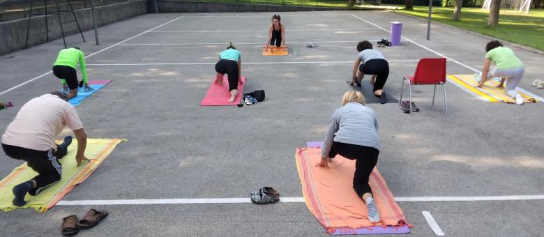 Lezione di yoga all'aperto con istruttrice e partecipanti su tappetini.