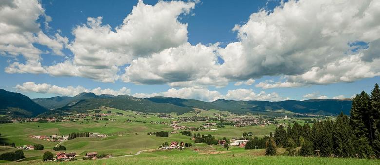 Paesaggio montano con cielo azzurro e nuvole bianche sopra una valle verde.