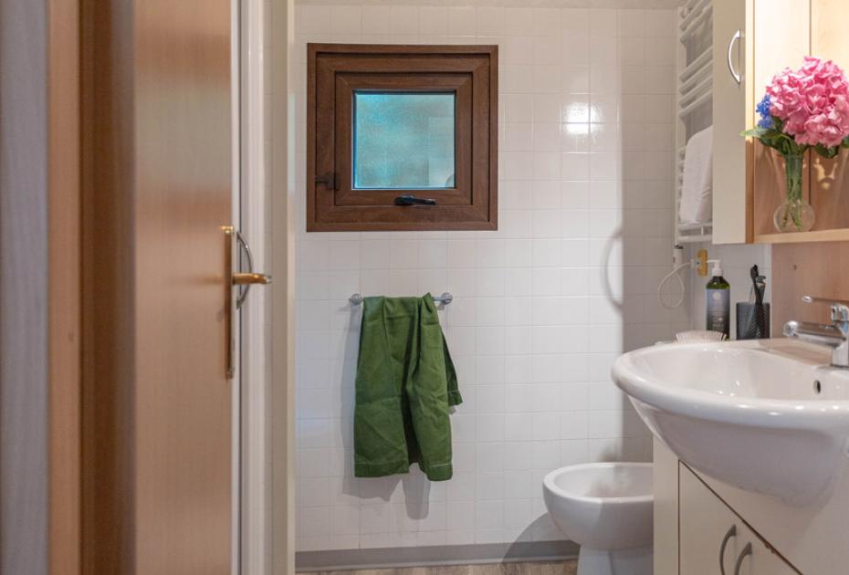 Bagno con lavabo, finestra, asciugamani verdi e fiori rosa.